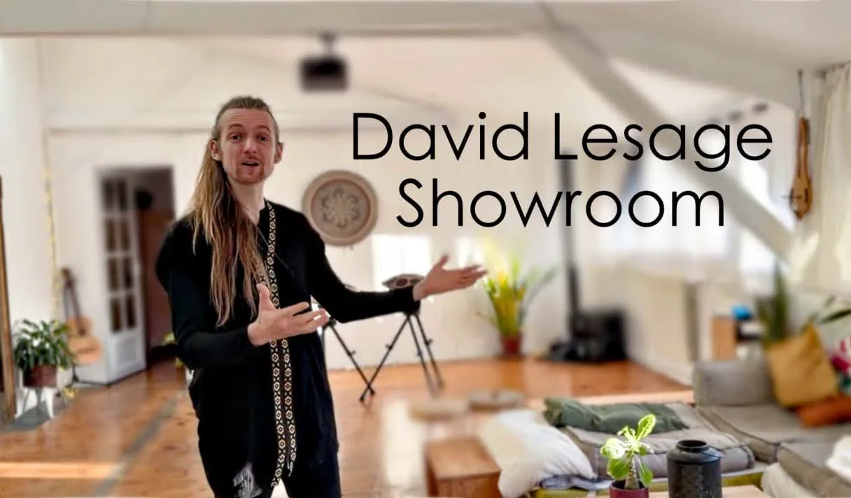 David Lesage, bras ouverts, accueille debout au milieu de la grande pièce du showroom : parquet ancien, murs blancs sous charpente, rosace au mur, un handpan sur son trépied derrière lui, des coussins et un canapé bas au fond. (Le titre « David Lesage Showroom » est incrusté sur l’image.)