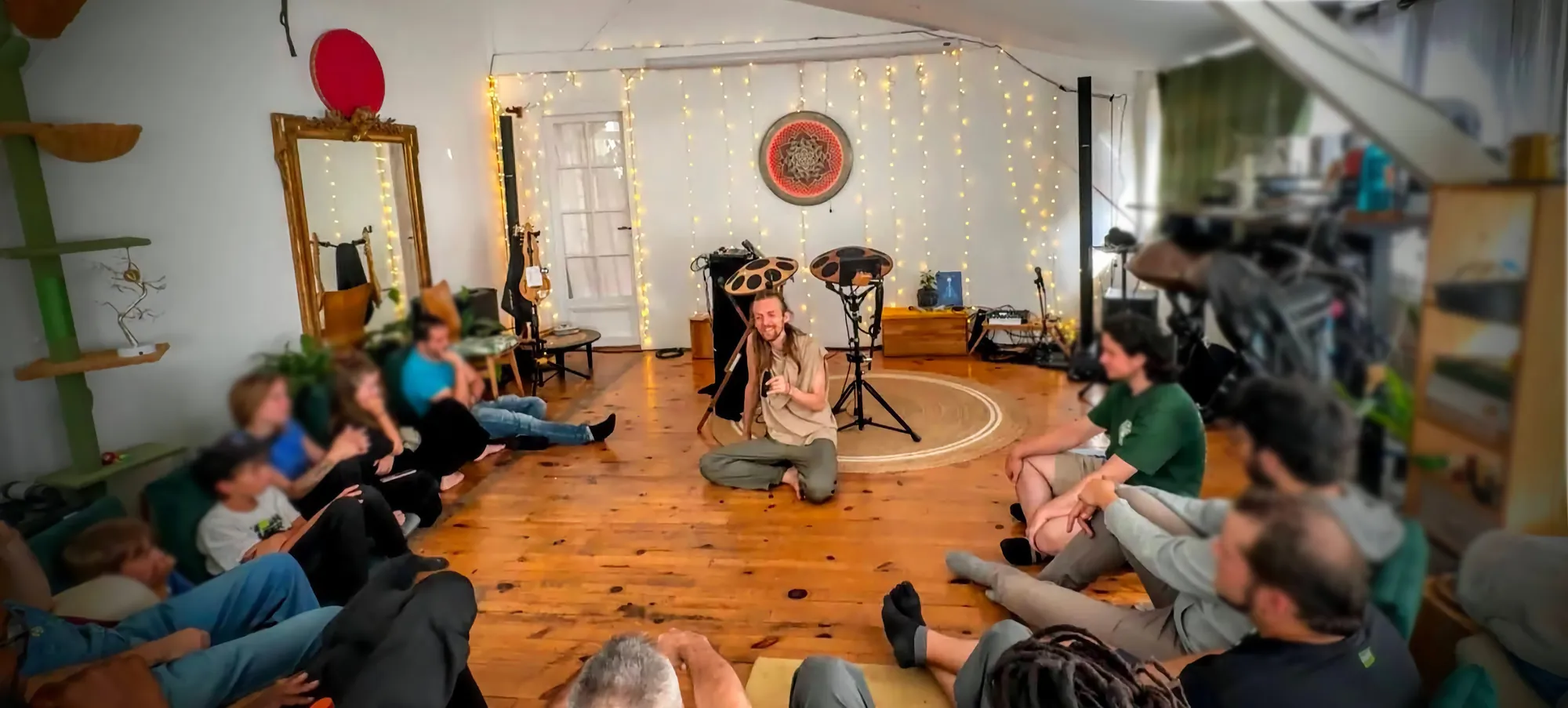 Vue d’ensemble d’un showcase au Nid : David Lesage assis au centre du cercle, handpans sur pieds derrière lui, le public assis à même le parquet, murs tendus de guirlandes lumineuses et rosace suspendue.