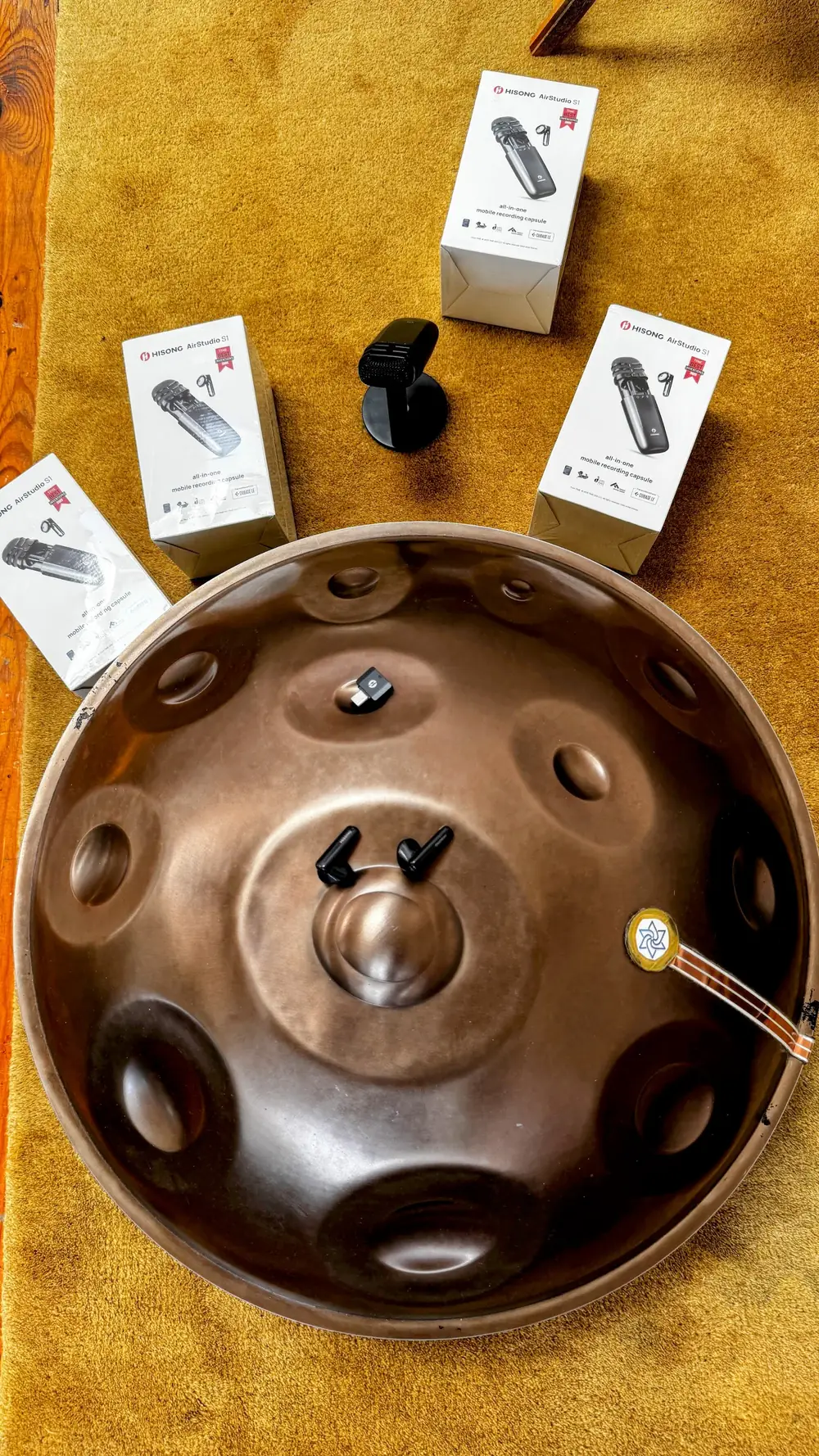 Un handpan Yishama vu de dessus, deux capsules de micro posées sur le dôme et quatre boîtes de micros Hisong AirStudio S1 disposées autour.